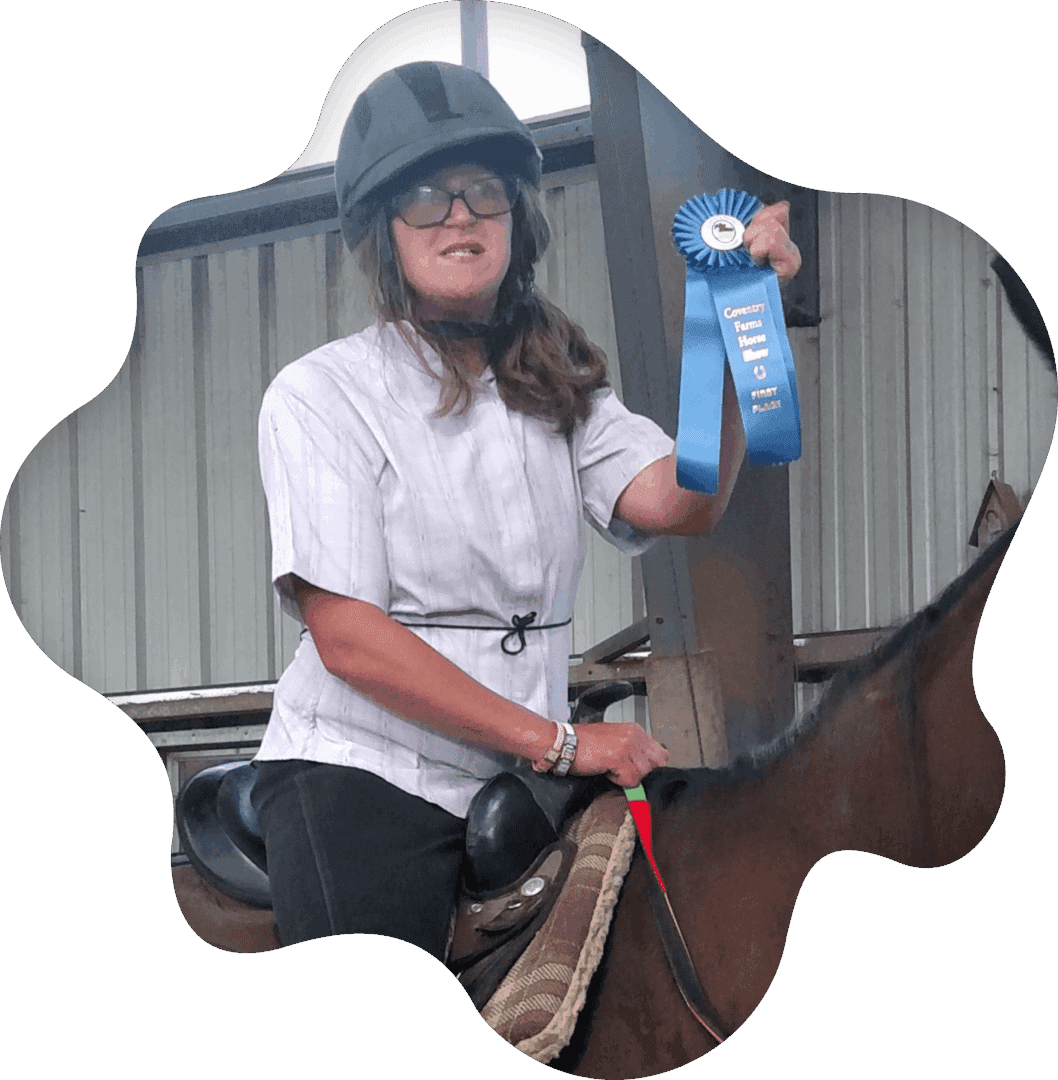 A smiling rider holding a blue ribbon on a horse.