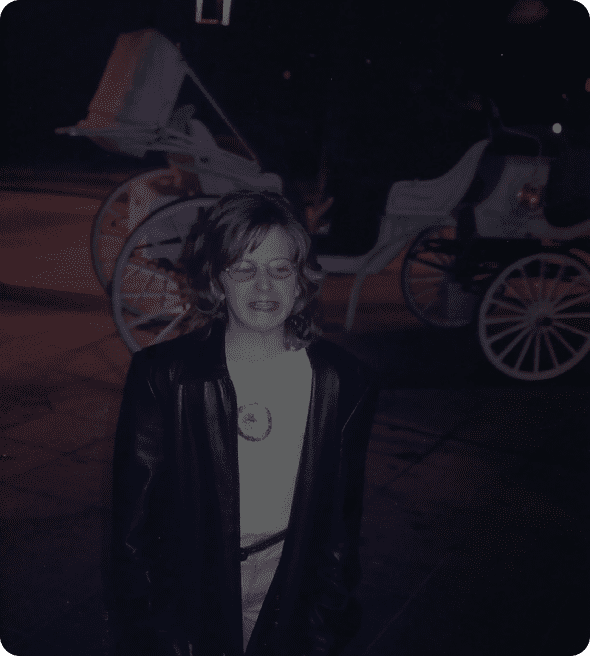 A person stands in front of a horse-drawn carriage at night.