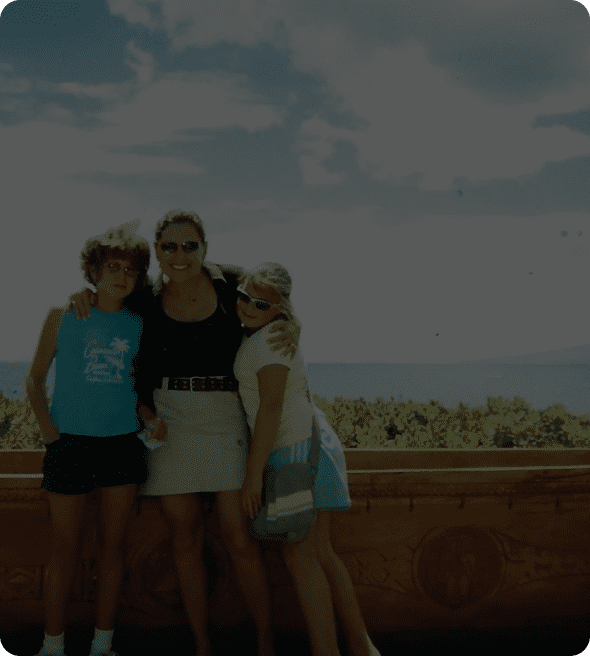 Three women standing together outdoors with a scenic background.